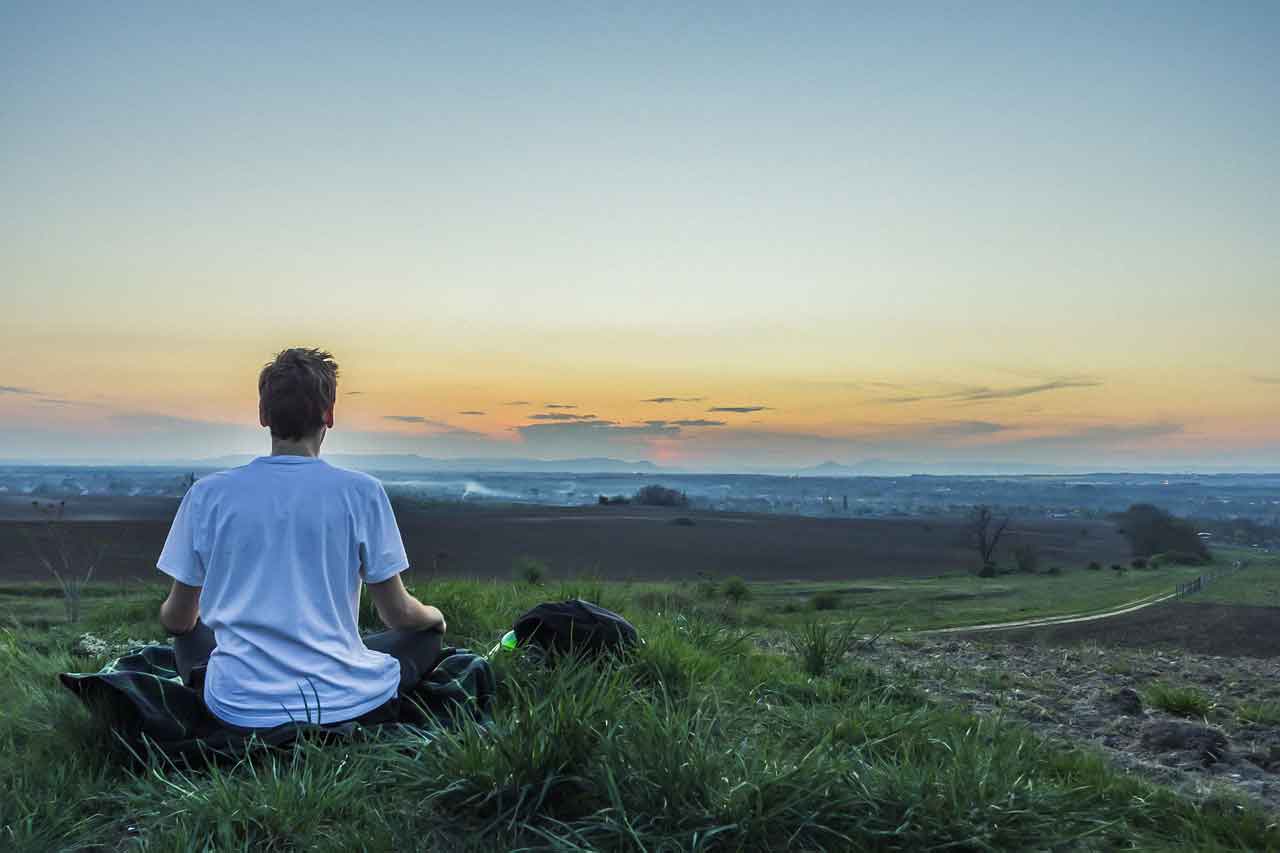 Junger Mann, der in der Abendsonne meditierend über ein Tal blickt