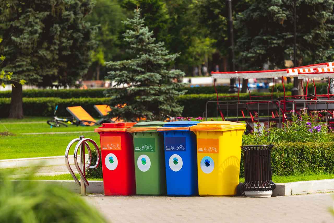 Vier bunte Mülltonnen in einer parkähnlichen Anlage